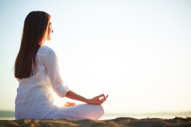 Zitting van de vrouw in yoga stelt op het strand