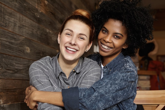 Zoet schot van gelukkig samesex vrouwelijk paar knuffelen, vrolijk lachen terwijl ze samen goede tijd doorbrengen in café