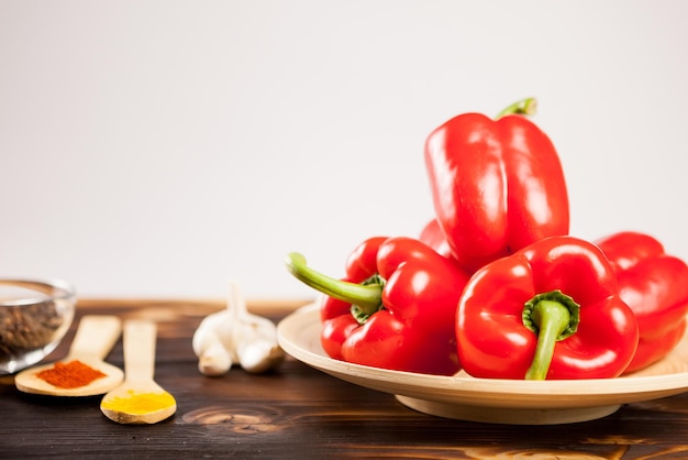 Zoete rode paprika's naast poederkruiden op een houten bord over grijze achtergrond