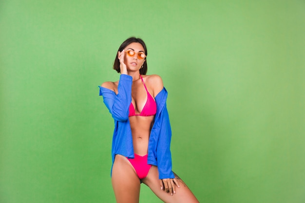 Zomer fit sportieve vrouw in roze bikini, blauw shirt en oranje zonnebril op groen, vrolijk vrolijk vrolijk positief