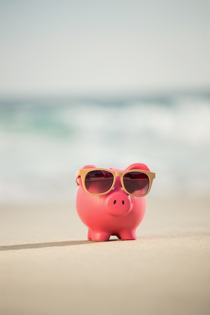 Gratis foto zomer spaarvarken met zonnebril op zand