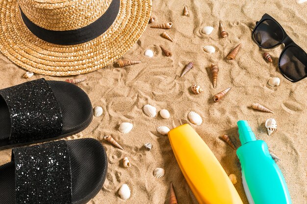 Zomer strandkleding, slippers, hoed, zonnebril en schelpen op zandstrand.