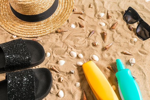 Zomer strandkleding, slippers, hoed, zonnebril en schelpen op zandstrand.