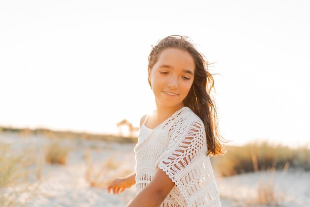 Zomerfoto van een klein meisje in een stijlvolle boho-outfit die op het strand poseert Warme zonsondergangkleuren Wacation en reisconcept