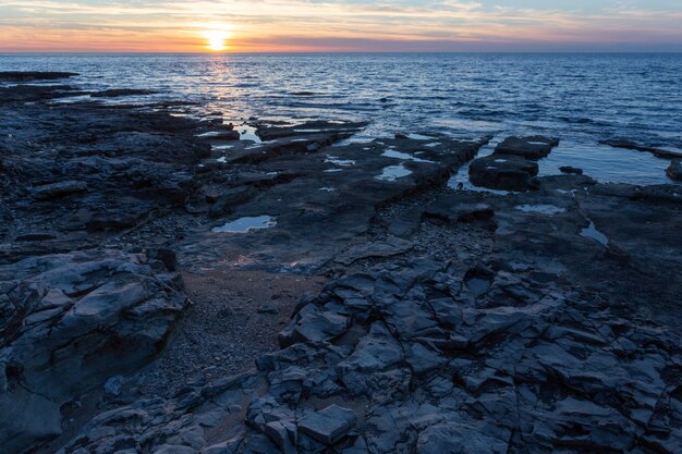 Zon die bij de kust met rotsvormingen plaatst in de Adriatische overzees in Savudrija, Istria, Kroatië