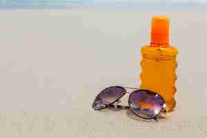 Gratis foto zonnebrandcrème lotion en een donkere bril op het strand voor de zomertijd