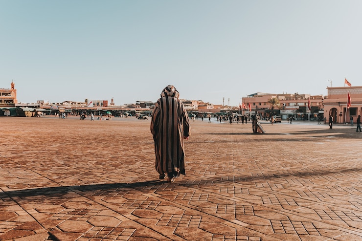 Gratis Foto zonnig landschap van een arabisch mannetje in gestripte thawb die in het grote stedelijke gebied loopt