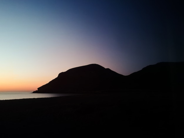 Zonsondergang met een silhouetberg op het strand