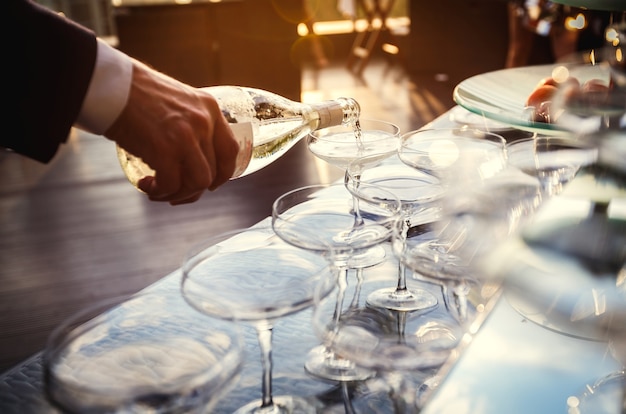 Zonsondergangclose-upmening van de hand van een kelner die mousserende wijn in glazen giet op een feestje. horeca en catering dienstverleningsconcept