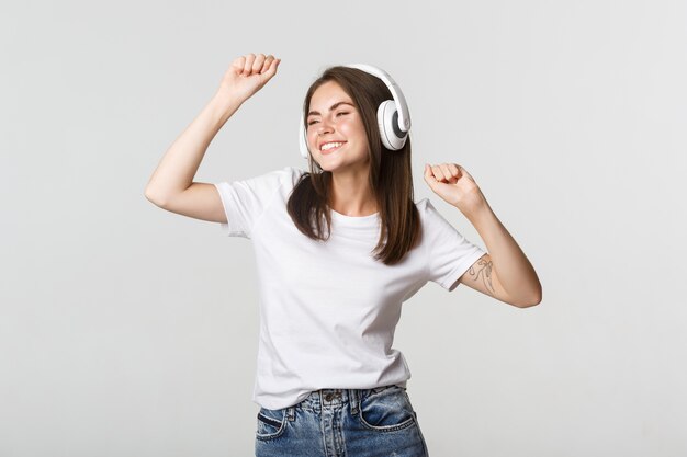 Zorgeloos aantrekkelijk meisje dansen en luisteren muziek in draadloze hoofdtelefoons.