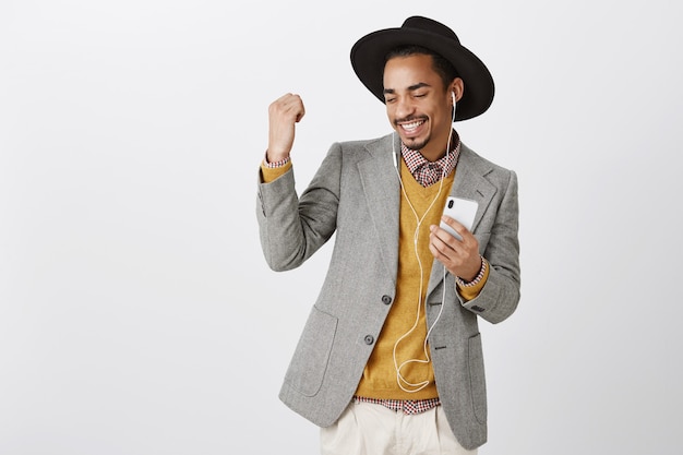 Zorgeloos dansende Afro-Amerikaanse man luisteren muziek in hoofdtelefoons, glimlachend en houden smartphone