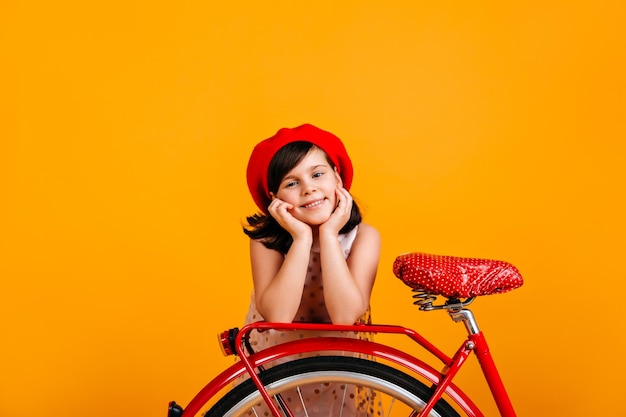 Zorgeloos kind in Franse baret poseren met fiets Studio shot van blanke preteen meisje geïsoleerd op geel