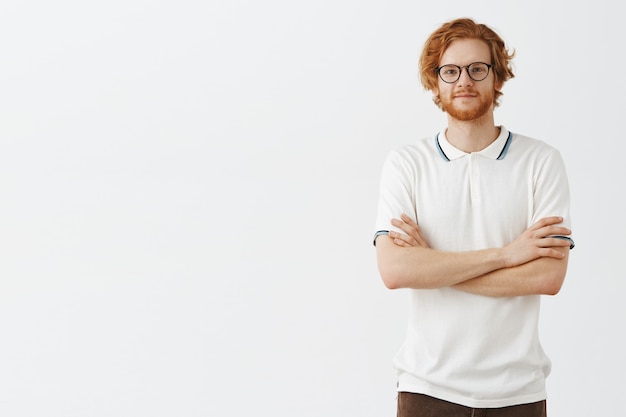 Zorgeloos knappe bebaarde roodharige man poseren tegen de witte muur met bril