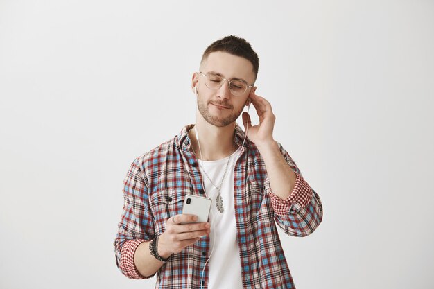 Zorgeloos lachende jonge man met een bril poseren met zijn telefoon