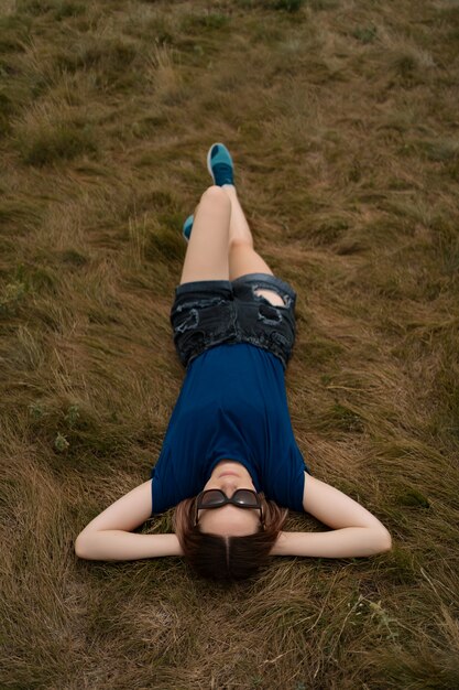 Zorgeloos vrouw ontspannen op het gras tijdens zonnige zomerdag met bril en korte broek.