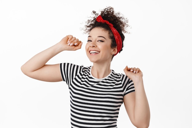 Zorgeloze aantrekkelijke vrouw in hoofdband, dansen en plezier maken, glimlachen en lachen ontspannen, rusten op een feestje, staande tegen een witte achtergrond.