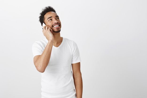Zorgeloze Afro-Amerikaanse man op zoek naar de rechterbovenhoek met een gelukkige glimlach tijdens het praten op de mobiele telefoon