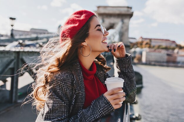 Zorgeloze blanke vrouw in rode hoed genieten van uitzicht op de stad op warme, winderige dag