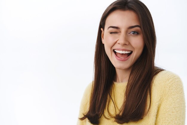 Zorgeloze brutale jonge brunette vrouw in gele trui, knipoog camera koket en glimlachend, verzeker alles geweldig, moedig aan om te genieten van een geweldige lentedag