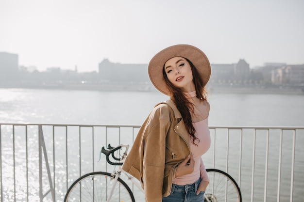 Zorgeloze gember vrouw in beige jas poseren in de buurt van fiets