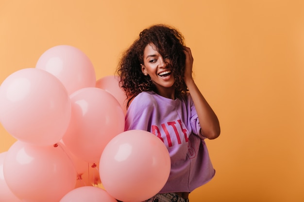 Zorgeloze jonge dame helium ballonnen houden op oranje en glimlachen. Lachend positief zwart meisje viert verjaardag.