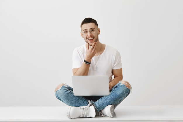 Zorgeloze jonge man met een bril poseren met zijn laptop