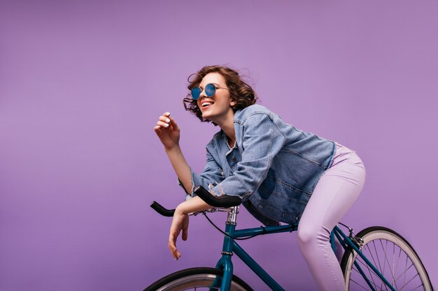 Zorgeloze kortharige dame zittend op de fiets. Gelukkig Kaukasisch meisje dat met golvend kapsel positieve emoties uitdrukt.