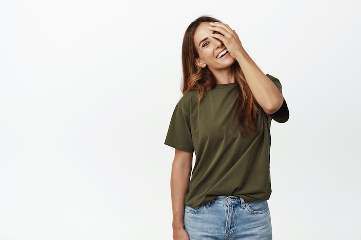 Gratis Foto zorgeloze vrouw van middelbare leeftijd met perfecte gezichtshuid, geen rimpels, gezond lang haar, haar gezicht aanraken, één oog bedekken en gelukkig lachend naar de camera, witte achtergrond