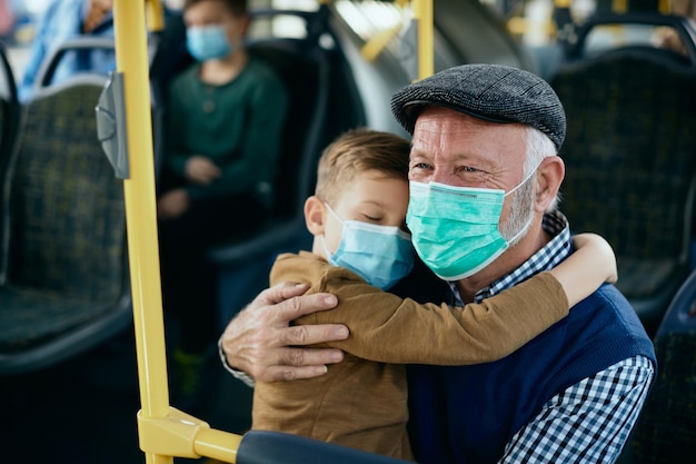 Zorgzame grootvader met kleinzoon die gezichtsmaskers draagt tijdens het woon-werkverkeer met de bus