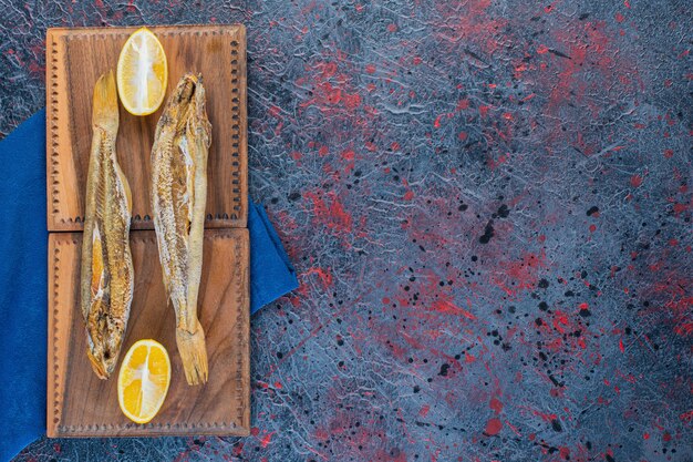Zoute gedroogde vis met een schijfje citroen geïsoleerd op een houten bord