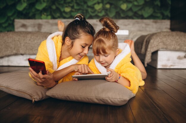 Zusters die op vloer met telefoon en tablet liggen