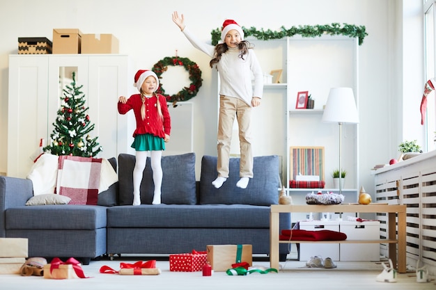 Zusters springen en spelen op de bank, meisjes met kerstmuts