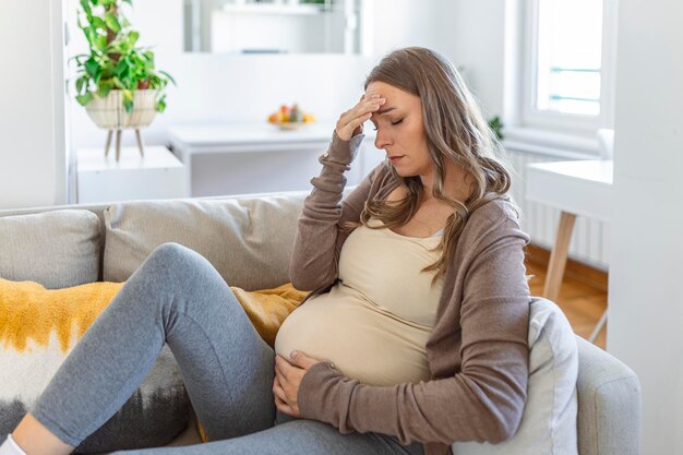 Zwangere jonge volwassen vrouw die op de bank thuis rust en zich onwel voelt jonge zwangere vrouw ziek