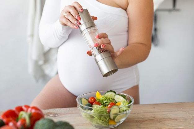 Gratis foto zwangere vrouw die haar salade kruiden