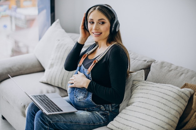 Zwangere vrouw die naar muziek luistert in oortelefoons en op internet surft