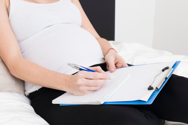 Zwangere vrouw die op klembord schrijft