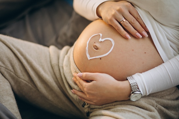 Gratis foto zwangere vrouw die room op de buik toepast om uitrekken te voorkomen