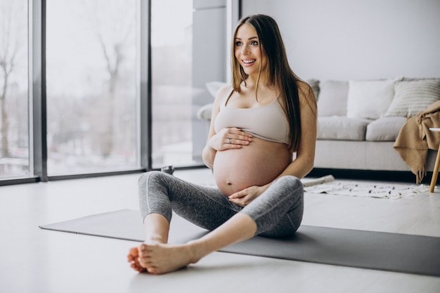 Zwangere vrouw die thuis yoga op mat beoefent