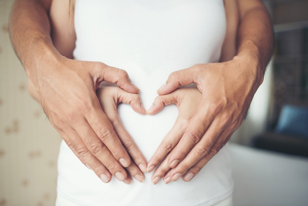 Zwangere vrouw en haar man hand tonen hart vorm.