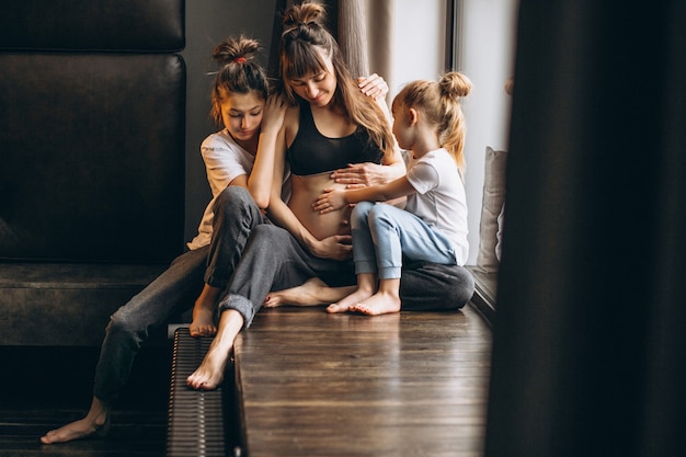 Zwangere vrouw met kinderen die bij het venster zitten