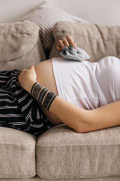 Zwangere vrouw met tatoeages houdt schoentjes voor haar baby en raakt de buik zachtjes aan