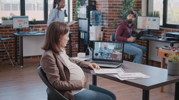 Zwangere werknemer die videogesprek gebruikt om met manager te praten over projectplanning en -strategie. Vrouw die een zakelijke bijeenkomst bijwoont met een collega op een online videoconferentie, in verwachting van een kind.
