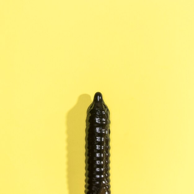 Zwart condoom op gele achtergrond met exemplaar-ruimte