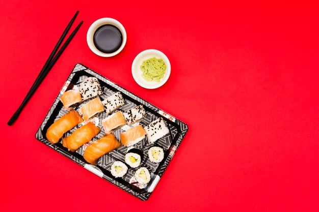Zwart dienblad met broodjes dichtbij wasabi en sojasaus op rode teller wordt gevuld die