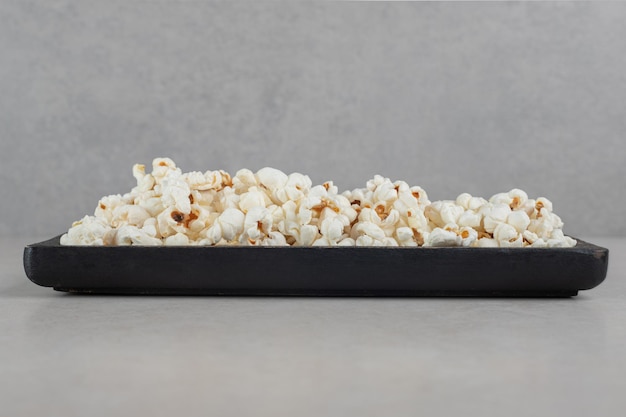 Zwart dienblad met popcorn op marmeren oppervlak.