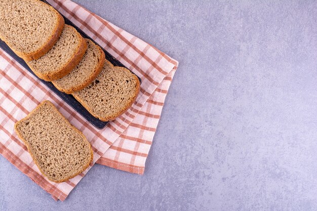 Zwart dienblad van gesneden bruin brood op een gevouwen handdoek op marmeren oppervlakte