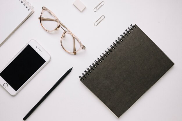 Zwart notitieboekje dichtbij smartphone en kantoorbehoeften