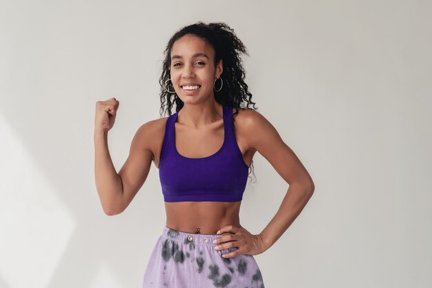 zwarte afro-amerikaanse vrouw in stijlvolle hipster fitness outfit violet top en broek op wit