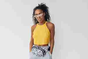 Gratis foto zwarte afro-amerikaanse vrouw in stijlvolle hipster-outfit gele top op wit