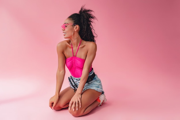 Zwarte afro-amerikaanse vrouw zit in een stijlvolle zomeroutfit roze top en korte broek heuptas op roze